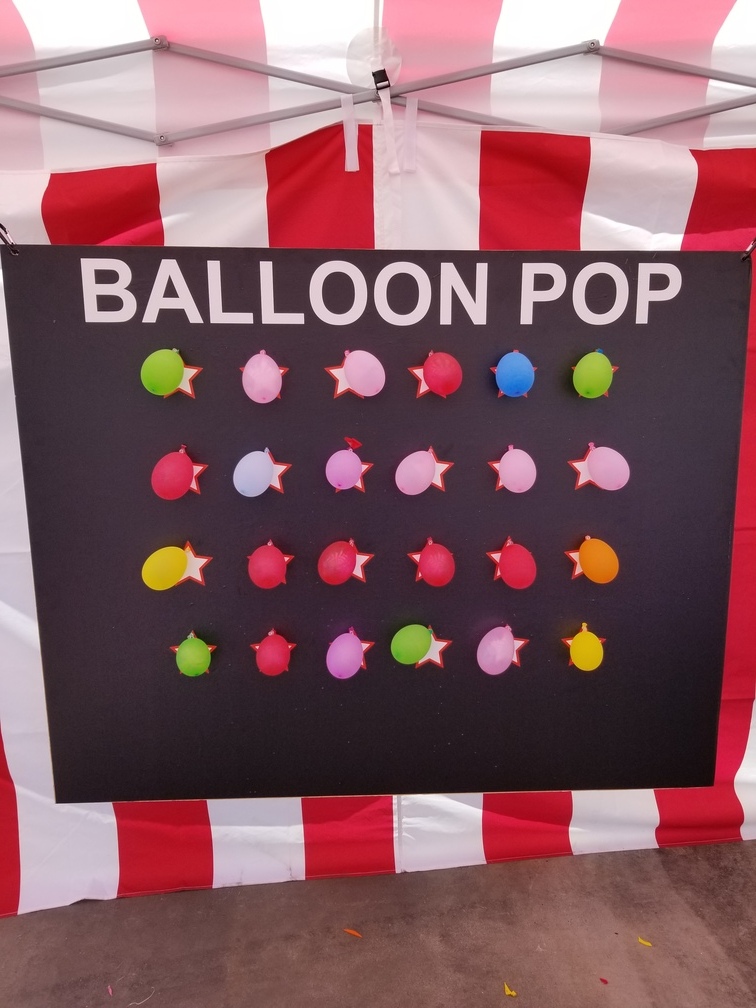Balloon pop dart-throwing carnival game with colourful balloons on a black board