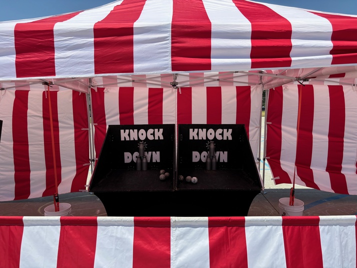 Forever Party Rentals carnival game booth — bottle knockdown under a red and white striped tent